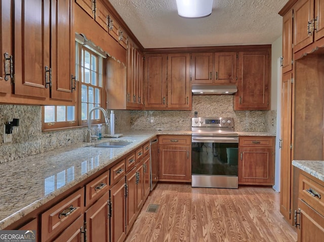 kitchen with stainless steel appliances, light wood-type flooring, light stone countertops, sink, and tasteful backsplash