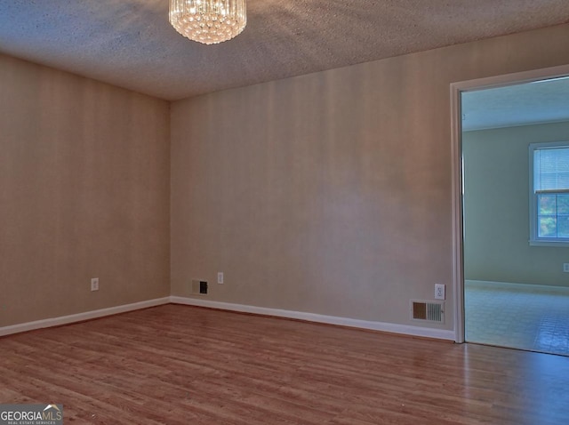 unfurnished room with a textured ceiling, a notable chandelier, and hardwood / wood-style floors