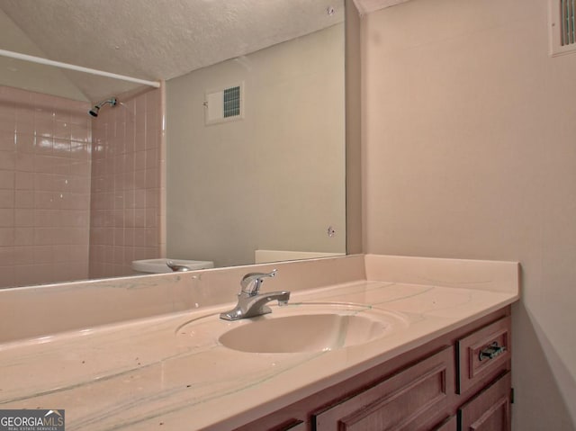 bathroom featuring vanity, a textured ceiling, and tiled shower