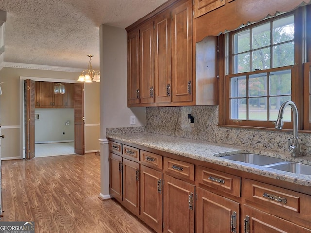 kitchen featuring light stone counters, a textured ceiling, a chandelier, light hardwood / wood-style floors, and sink