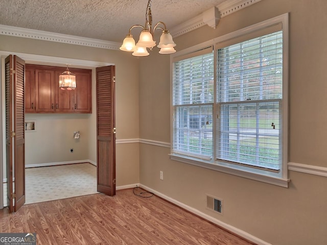 unfurnished dining area featuring an inviting chandelier, ornamental molding, a textured ceiling, and light wood-type flooring