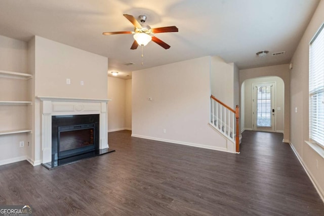 unfurnished living room featuring ceiling fan, built in features, and dark wood-type flooring