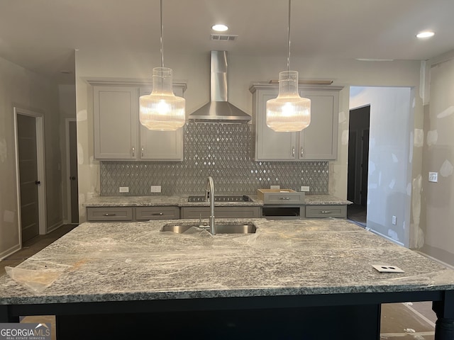 kitchen featuring an island with sink, wall chimney exhaust hood, and pendant lighting