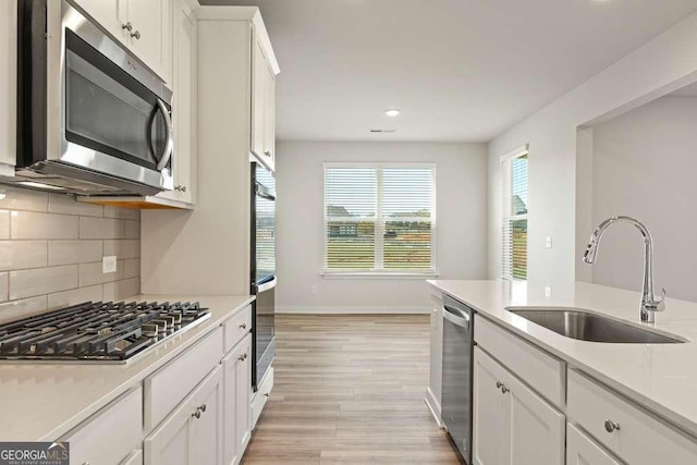 kitchen featuring stainless steel appliances, light wood-type flooring, decorative backsplash, sink, and white cabinetry