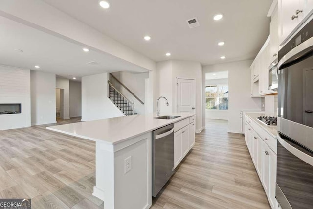 kitchen with a large fireplace, a center island with sink, appliances with stainless steel finishes, sink, and white cabinetry