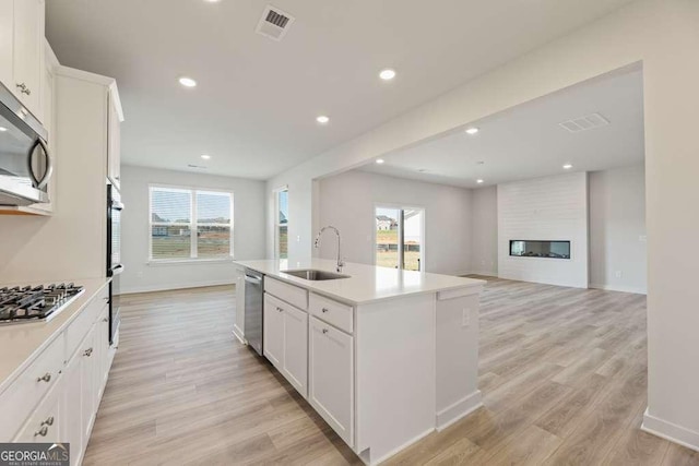 kitchen featuring sink, stainless steel appliances, white cabinets, a fireplace, and an island with sink