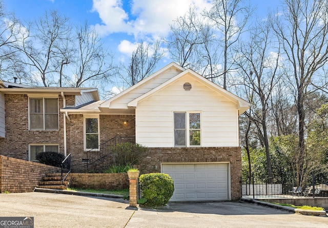 tri-level home featuring aphalt driveway, brick siding, an attached garage, and fence