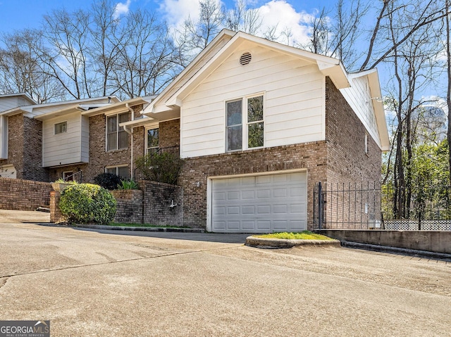 view of front of house featuring an attached garage, fence, brick siding, and driveway