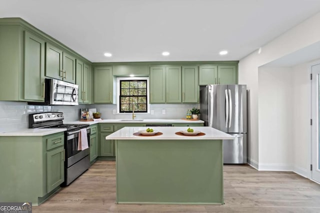 kitchen with stainless steel appliances, green cabinets, a center island, and light wood-type flooring