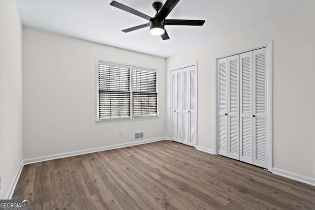 unfurnished bedroom featuring two closets, ceiling fan, and hardwood / wood-style floors