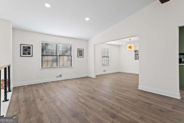 unfurnished living room featuring a notable chandelier, vaulted ceiling, and wood-type flooring