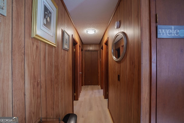 corridor featuring a textured ceiling, wood walls, and light wood-type flooring