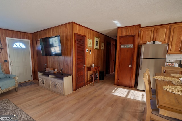 kitchen featuring a textured ceiling, light hardwood / wood-style flooring, wooden walls, and stainless steel refrigerator