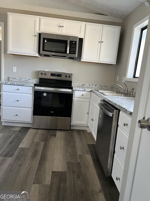 kitchen featuring dark wood-type flooring, light stone countertops, stainless steel appliances, white cabinets, and sink