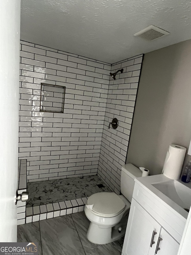 bathroom with toilet, tiled shower, a textured ceiling, and vanity