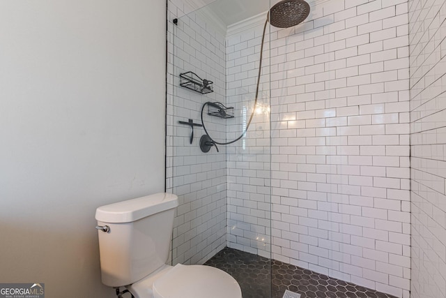 bathroom featuring toilet, a tile shower, and crown molding