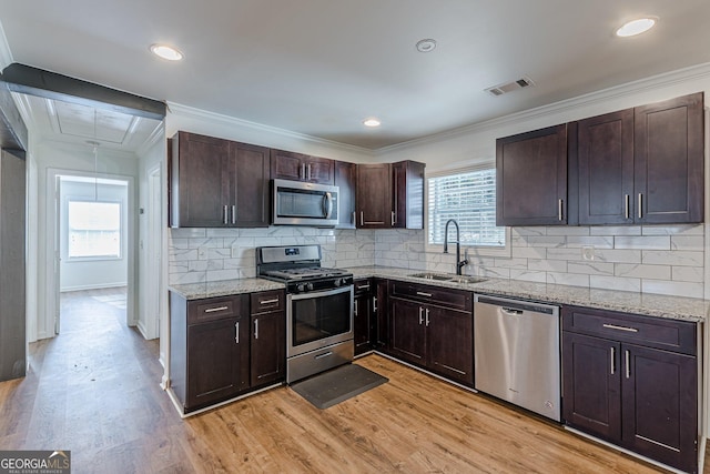 kitchen featuring appliances with stainless steel finishes, light stone countertops, dark brown cabinetry, sink, and light hardwood / wood-style flooring