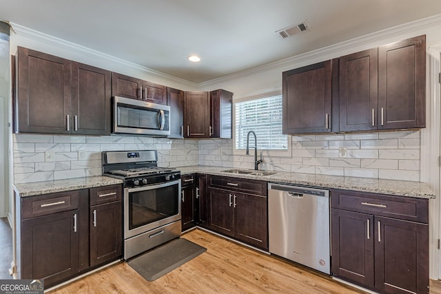 kitchen featuring stainless steel appliances, sink, tasteful backsplash, dark brown cabinetry, and light stone countertops