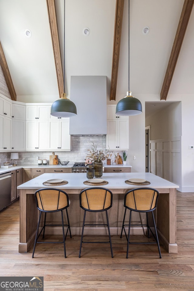 kitchen featuring a breakfast bar area, decorative light fixtures, dishwasher, white cabinets, and beamed ceiling