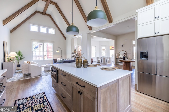 kitchen with stainless steel fridge, light wood-type flooring, high vaulted ceiling, pendant lighting, and white cabinets