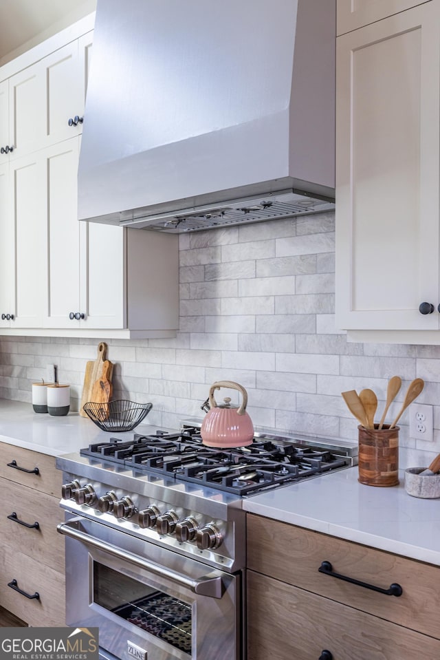 kitchen featuring backsplash, stainless steel stove, white cabinets, and wall chimney exhaust hood