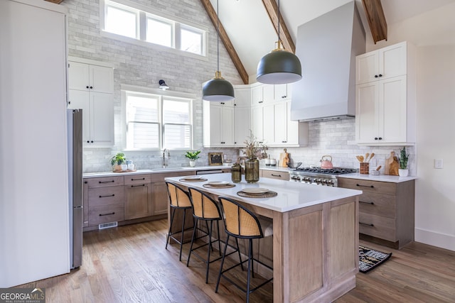 kitchen with wall chimney range hood, a center island, hanging light fixtures, high vaulted ceiling, and white cabinets