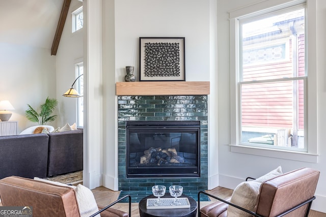 living room with plenty of natural light, light hardwood / wood-style floors, a tiled fireplace, and lofted ceiling with beams