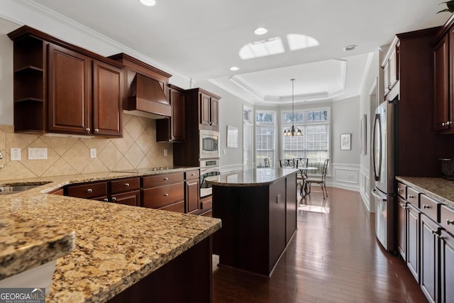 kitchen with appliances with stainless steel finishes, a center island, custom range hood, a tray ceiling, and sink