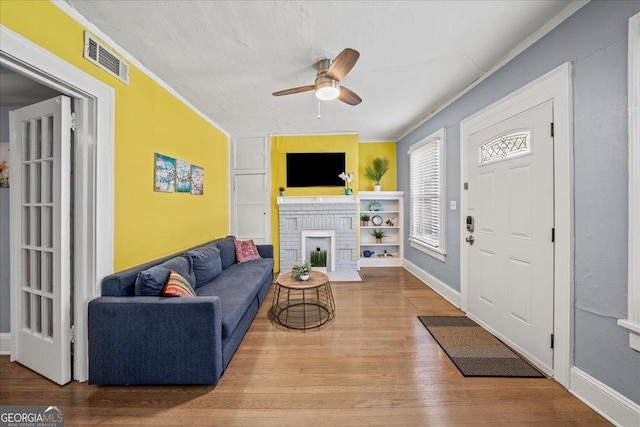 living room featuring ceiling fan, a fireplace, hardwood / wood-style floors, a textured ceiling, and ornamental molding