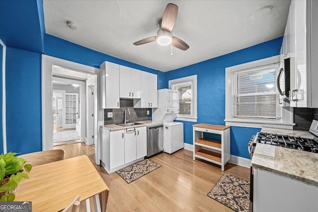 kitchen featuring stacked washer and clothes dryer, stainless steel appliances, tasteful backsplash, white cabinets, and sink