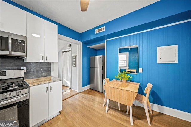 kitchen with white cabinetry, appliances with stainless steel finishes, backsplash, light hardwood / wood-style flooring, and light stone counters