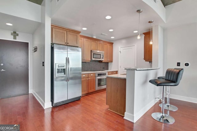 kitchen with appliances with stainless steel finishes, kitchen peninsula, light stone countertops, decorative backsplash, and decorative light fixtures