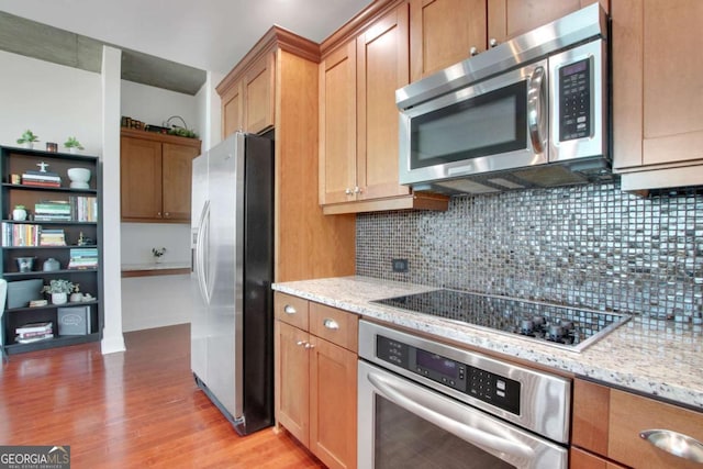 kitchen with light stone counters, stainless steel appliances, light hardwood / wood-style flooring, and backsplash