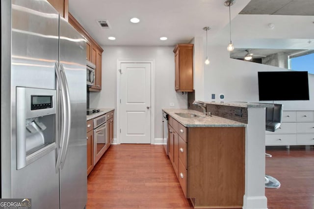 kitchen featuring stainless steel appliances, sink, decorative light fixtures, a breakfast bar area, and light stone countertops