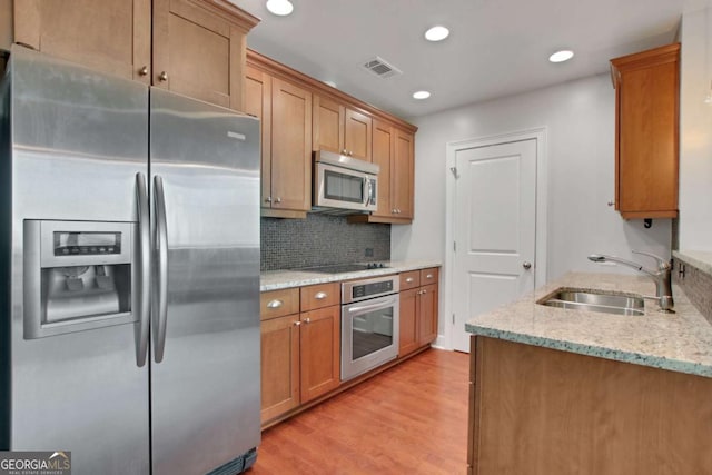 kitchen with stainless steel appliances, light wood-type flooring, light stone countertops, and sink