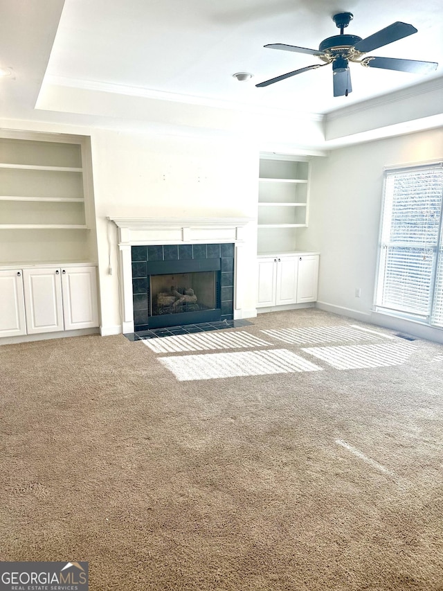 unfurnished living room with a fireplace, built in shelves, and a tray ceiling