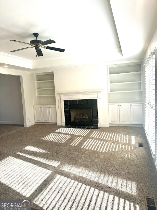 unfurnished living room featuring a fireplace, a raised ceiling, built in features, and ceiling fan