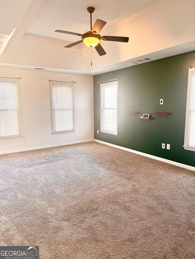 empty room with ceiling fan, a raised ceiling, and carpet