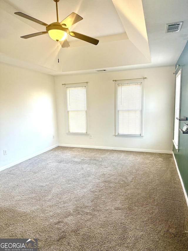 carpeted spare room with ceiling fan, a tray ceiling, and plenty of natural light