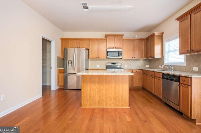 kitchen with sink, light wood-type flooring, appliances with stainless steel finishes, and a center island