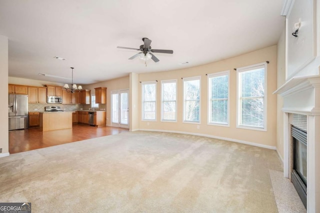 unfurnished living room with light colored carpet, a high end fireplace, and ceiling fan with notable chandelier