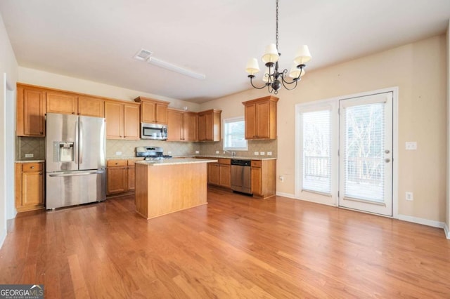 kitchen with stainless steel appliances, decorative light fixtures, a center island, an inviting chandelier, and light hardwood / wood-style floors