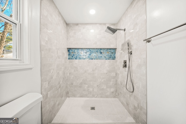 bathroom with a tile shower and toilet