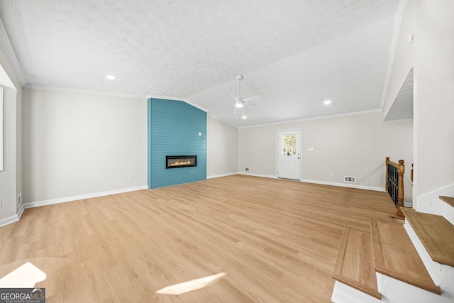 unfurnished living room featuring a large fireplace, a textured ceiling, vaulted ceiling, ornamental molding, and ceiling fan