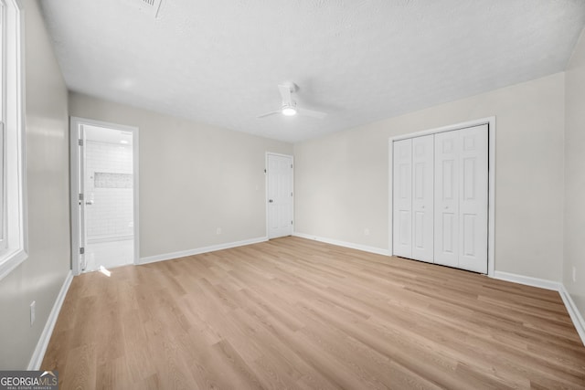 unfurnished bedroom featuring a textured ceiling, ensuite bathroom, a closet, light hardwood / wood-style floors, and ceiling fan