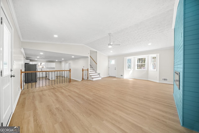 unfurnished living room featuring a textured ceiling, vaulted ceiling, ceiling fan, light wood-type flooring, and crown molding