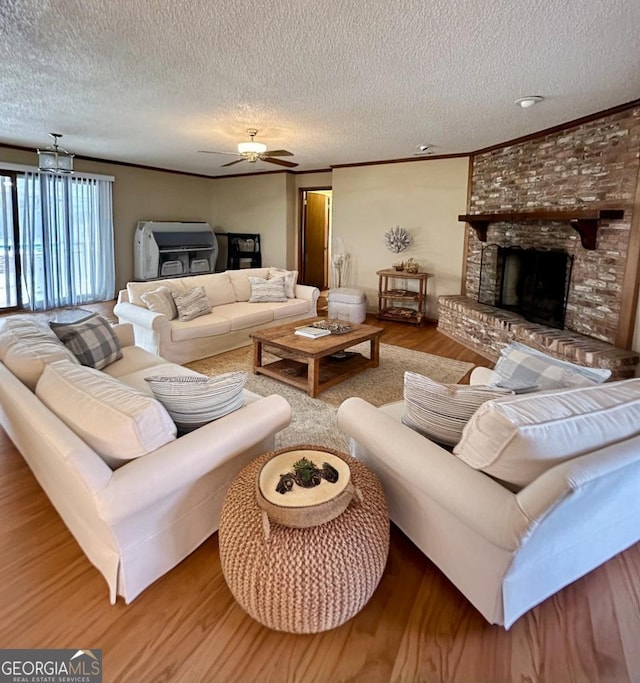 living room featuring hardwood / wood-style floors, ceiling fan, ornamental molding, a brick fireplace, and a textured ceiling