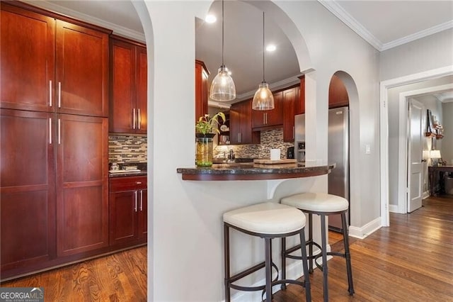 kitchen with ornamental molding, a breakfast bar area, decorative backsplash, dark hardwood / wood-style flooring, and pendant lighting