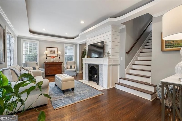 living room featuring hardwood / wood-style flooring, a large fireplace, a tray ceiling, and ornamental molding