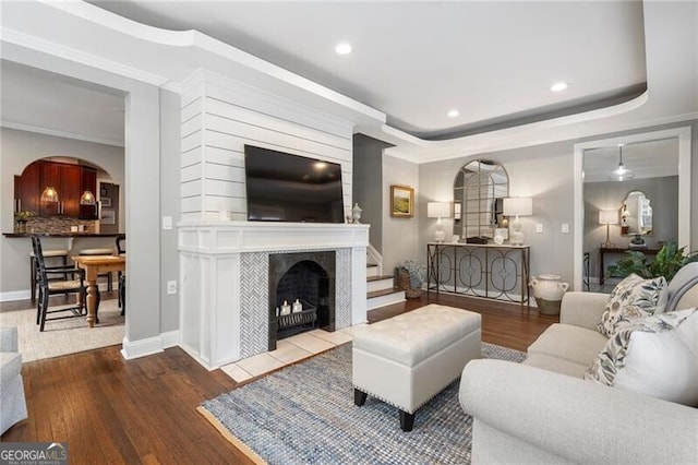 living room with crown molding, a tile fireplace, a tray ceiling, and hardwood / wood-style flooring